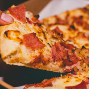 Close-up of a hand holding a delicious slice of pepperoni pizza.