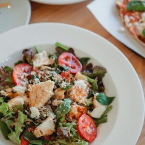 High angle of appetizing salad with fresh vegetables and meat under cheese on wooden table in restaurant