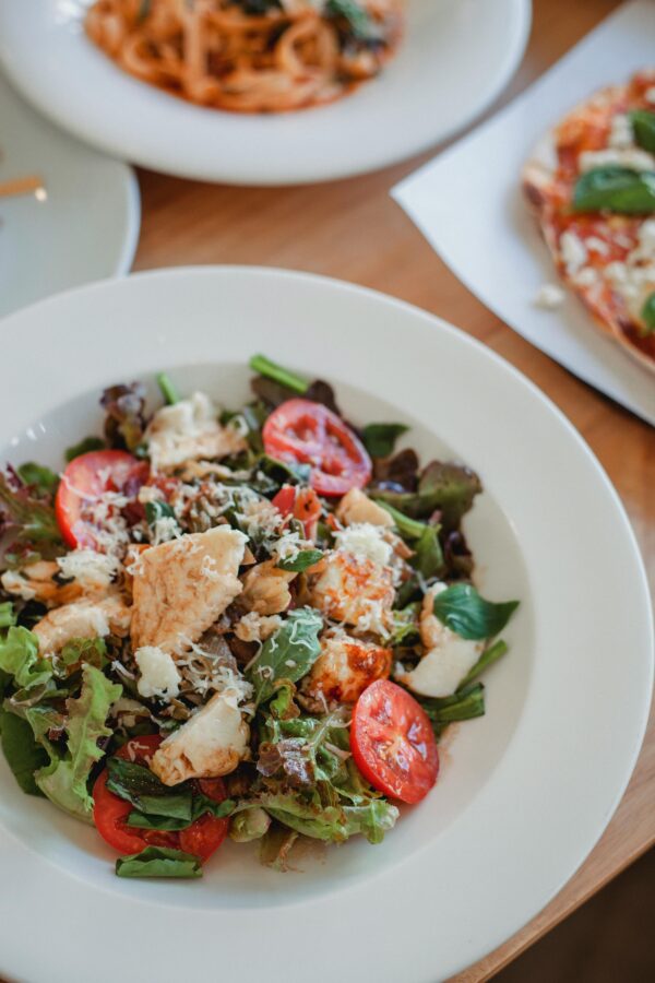 High angle of appetizing salad with fresh vegetables and meat under cheese on wooden table in restaurant
